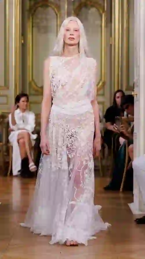 Close-up of an intricately embroidered white lace gown at a fashion show.