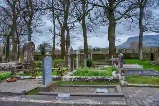 WB Yeats' grave surrounded by historic headstones and bare trees in a peaceful churchyard in County Sligo, Ireland.