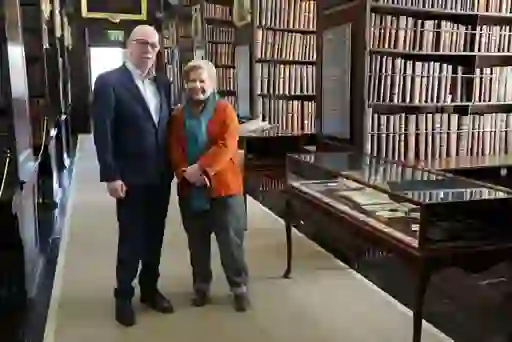 Sandi Toksvig and a man stand beside glass display cases and shelves of historic books in Marsh's Library, Dublin.