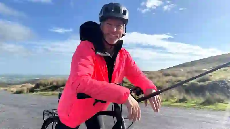 Fred Siriex resting on a bike on a rural road in the Comeragh Mountains, County Waterford, with rolling hills and blue sky behind.