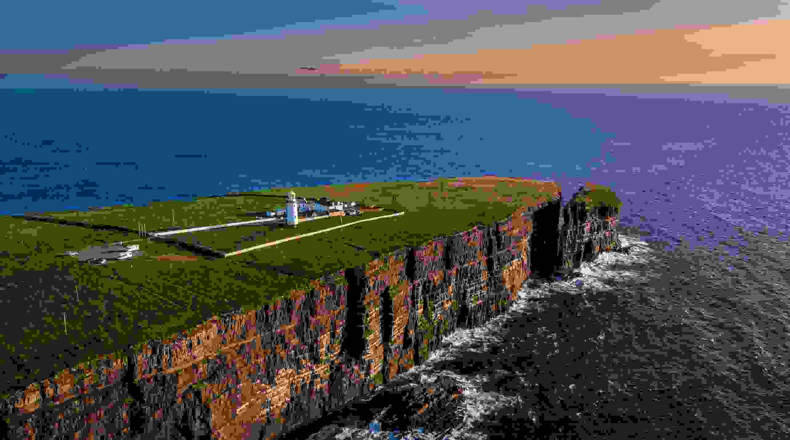 Der Loop Head Lighthouse vor atemberaubender Landschaft, mit Klippen und tollem Sonnenuntergang.
