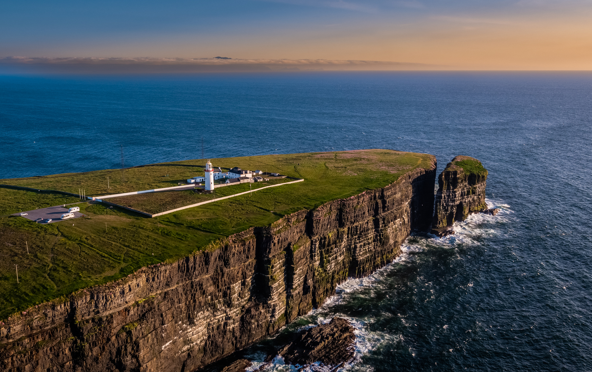 Der Loop Head Lighthouse vor atemberaubender Landschaft, mit Klippen und tollem Sonnenuntergang.