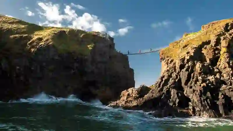 Visitors crossing the Carrick-a-Rede-rope bridge in County Antrim between rugged sea cliffs above crashing Atlantic waves.