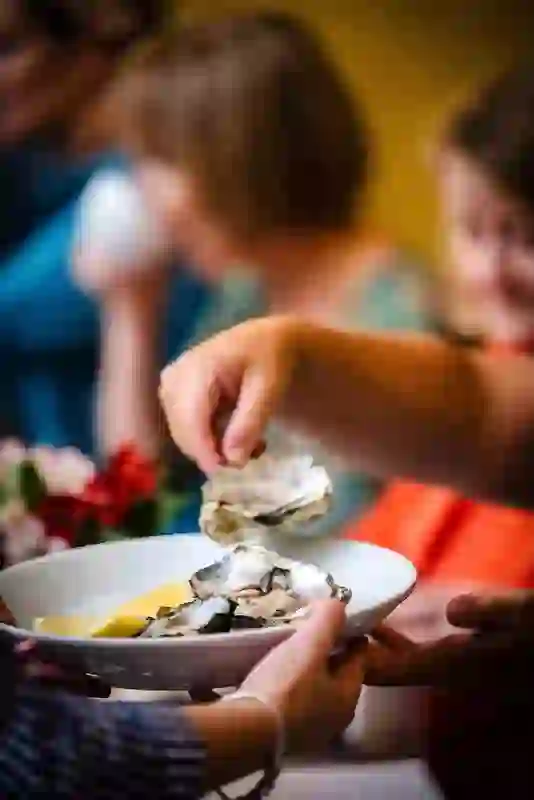 Hands passing a bowl of fresh oysters with lemon wedges at the busy English Market in Cork city.