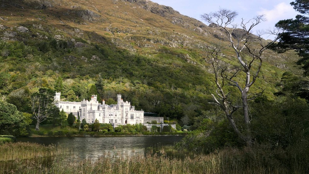 Kylemore Abbey reflected in a Connemara lake, surrounded by forested hills in County Galway.