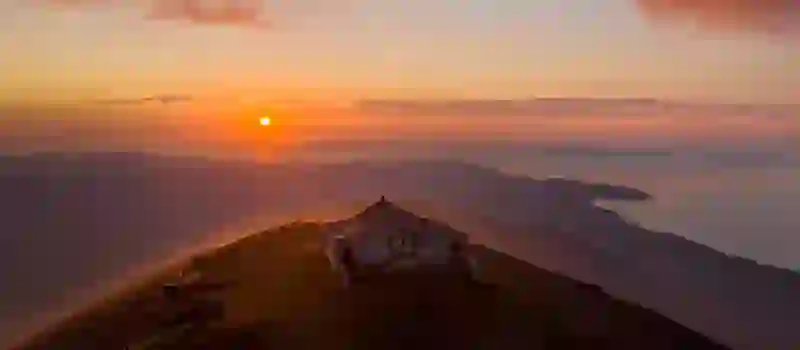 Small chapel sits atop a misty Croagh Patrick mountain at sunrise, with dramatic views of Clew Bay below and orange skies above.