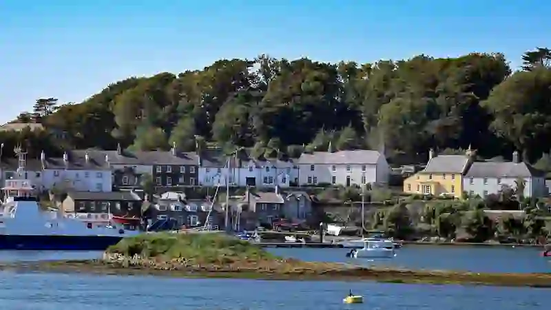 Boats and a ferry sit in Strangford Harbour with colourful village houses along the waterfront, County Down.