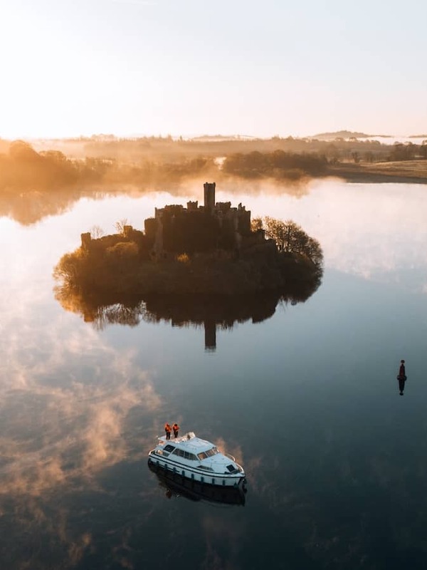 Boat glides across calm Lough Key at sunrise with a castle island emerging through soft mist, County Roscommon.