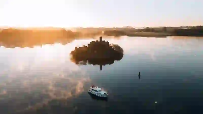 Boat glides across calm Lough Key at sunrise with a castle island emerging through soft mist, County Roscommon.