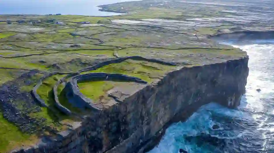 Ancient stone fort perched on sea cliffs of the Aran island of Inis Mór, County Galway surrounded by green fields and rugged Atlantic coastline.