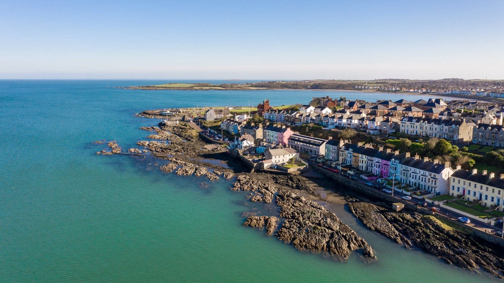 A row of colourful houses lines a rocky coastline in Bangor, County Down, backed by a sheltered bay and gentle headlands.