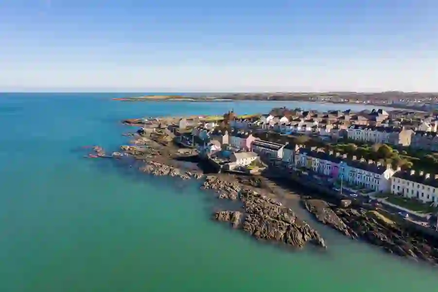 A row of colourful houses lines a rocky coastline in Bangor, County Down, backed by a sheltered bay and gentle headlands.
