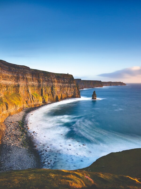Blarney Castle surrounded by autumn trees and gardens in County Cork, Ireland, under a clear blue sky.