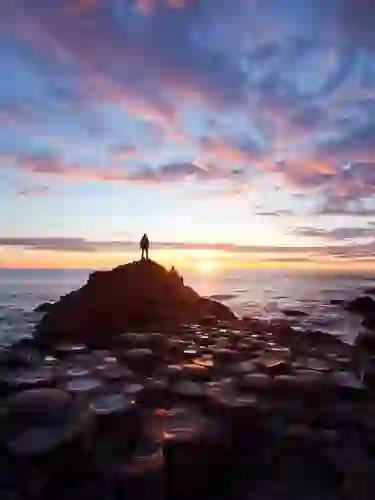 Person standing on Giant’s Causeway basalt columns at sunset, County Antrim.