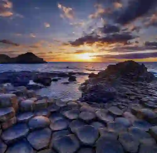 Sunset over the Giant’s Causeway, County Antrim, with hexagonal basalt stones and waves along the shore.