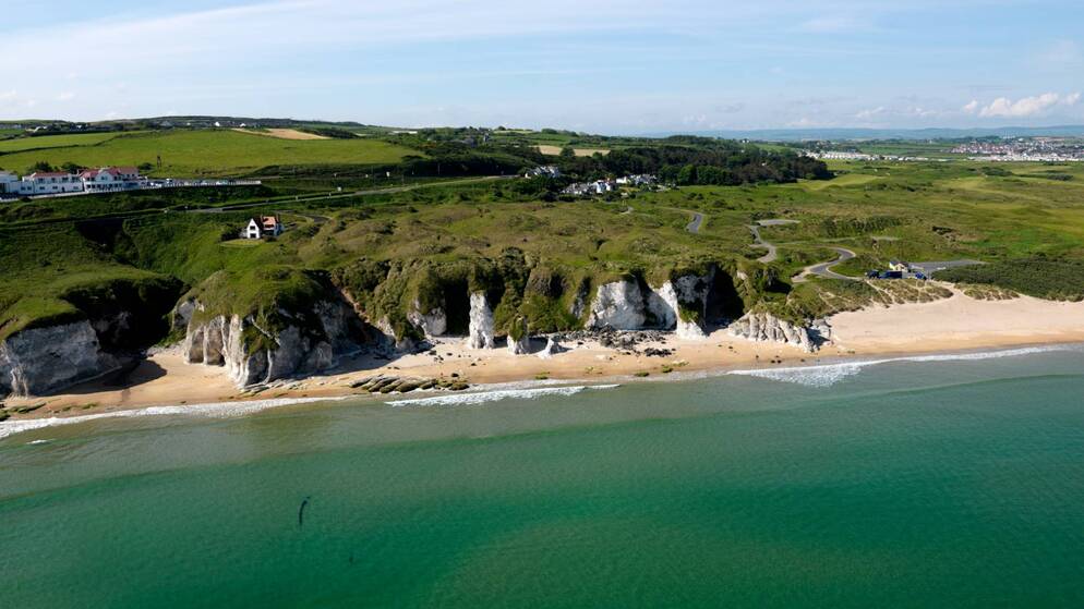 White sandy beach backed by cliffs near Portrush in County Antrim with walking trails leading along the coastline.