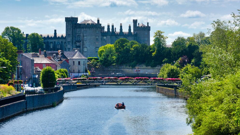 Kilkenny Castle overlooking the River Nore with floral bridge and people boating in Kilkenny City.