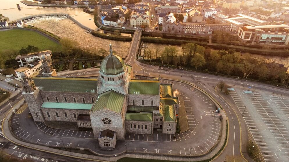 Aerial view of Galway Cathedral at sunset with River Corrib and city streets in the background.