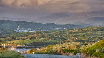 Peaceful rural village landscape with church spire and mountains, promoting B&B stays in the Irish countryside.