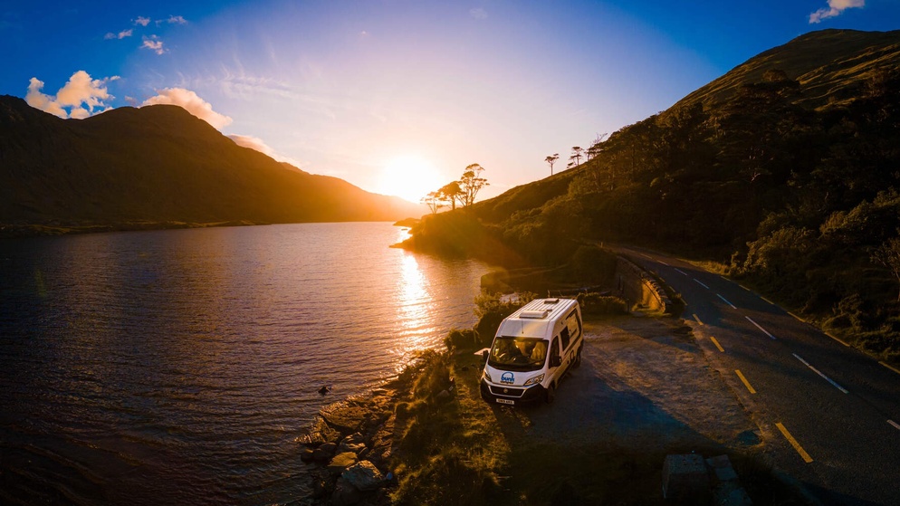 Campervan travelling at sunset along a scenic road by Lough Doo in County Mayo.