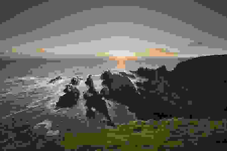 Il sole tramonta dietro le scogliere frastagliate e le onde che si infrangono sulla pittoresca costa di Cork.