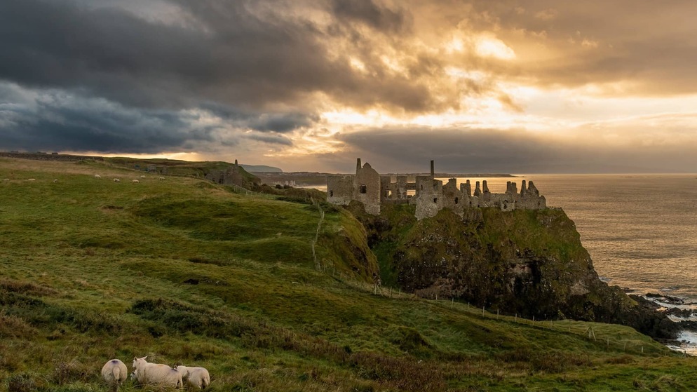 Die Ruinen der Burg Dunluce befinden sich am Rande einer Klippe über dem Meer bei Sonnenuntergang auf der Causeway Coastal Route.