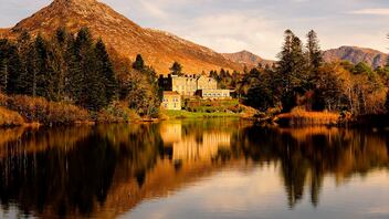 Grand lakeside hotel, Ballynahinch Castle, framed by autumn trees and mountains in the scenic Galway countryside.