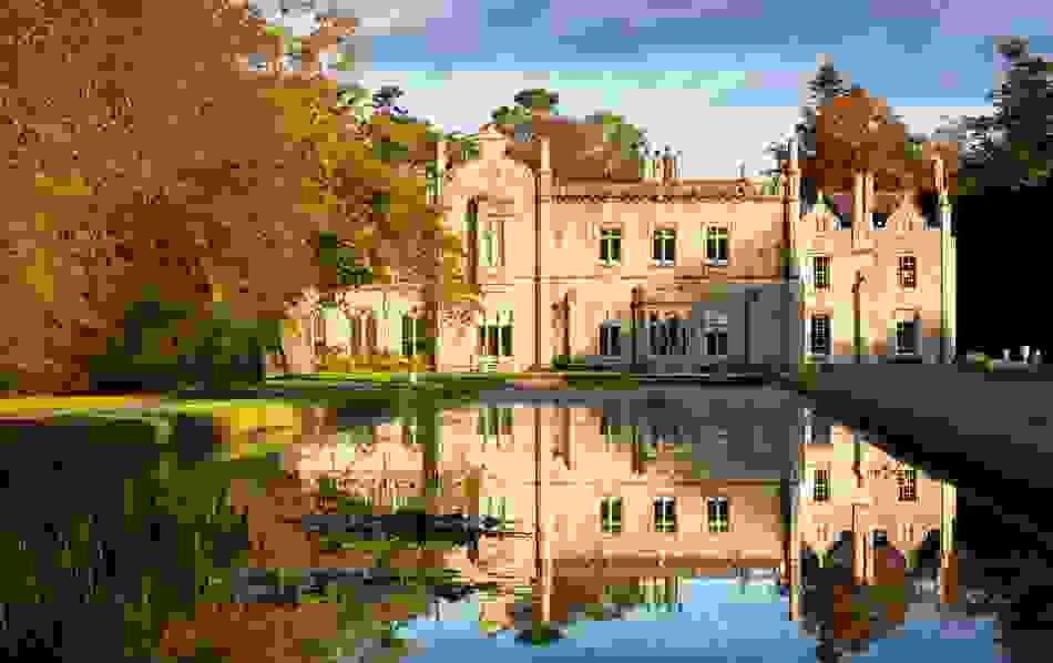 Historic stone mansion, Killruddery House, County Wicklow, reflecting on a still pond surrounded by autumn trees.