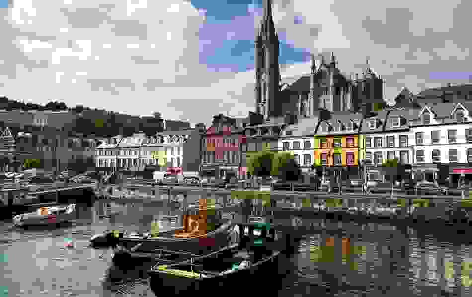 Colourful houses and fishing boats at Cobh Harbour, County Cork, with St Colman’s Cathedral in the background.