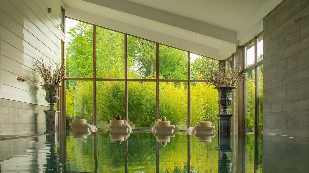 Bright spa lounge with tall windows, cushioned chairs and garden view framed by large vases.