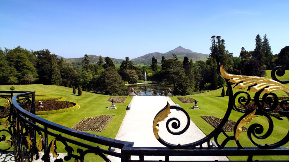 Ornamental gardens with mountain backdrop, fountains, and manicured lawns.