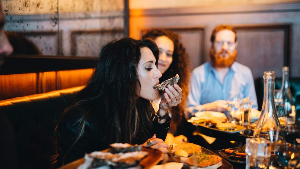 Woman tasting a fresh oyster on an Irish food tour with friends at a restaurant.