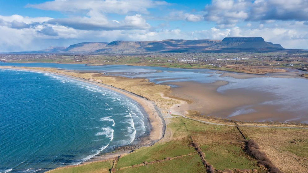 Aerial view of the coastline in County Sligo, with blue ocean, sandy shore, and Ben Bulben mountain in the background.