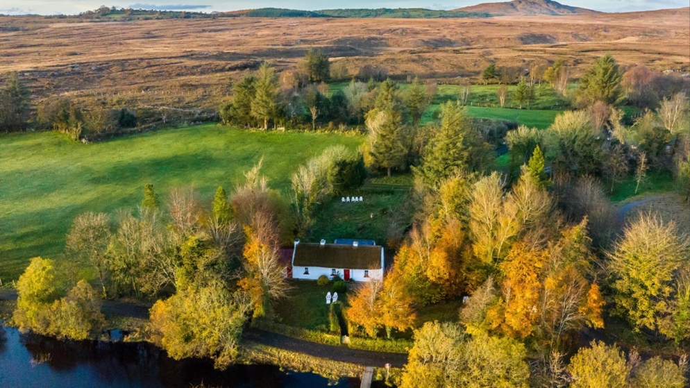 Keenaghan Cottage beside a lakeshore, surrounded by autumn trees, with rolling bogland and a distant mountain in County Fermanagh.