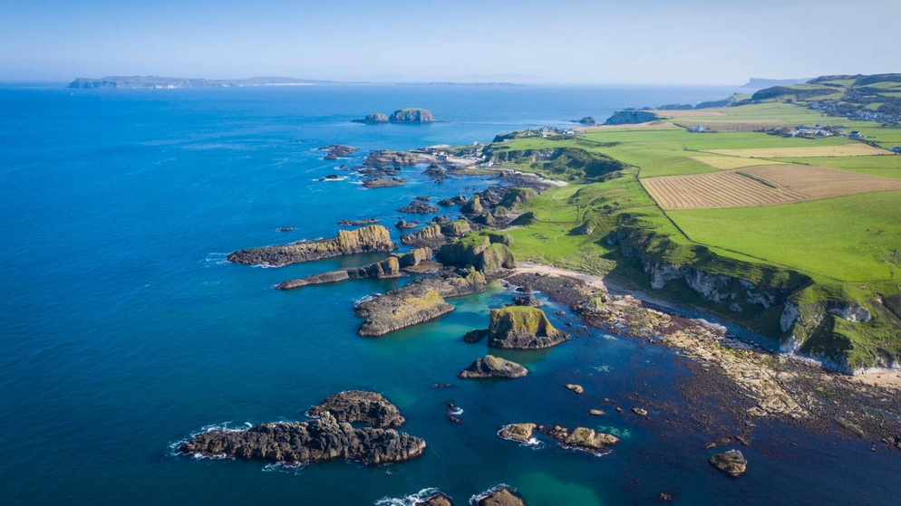 Aerial view of dramatic cliffs and green fields along the Causeway Coast, County Antrim, with rocky outcrops and blue sea.