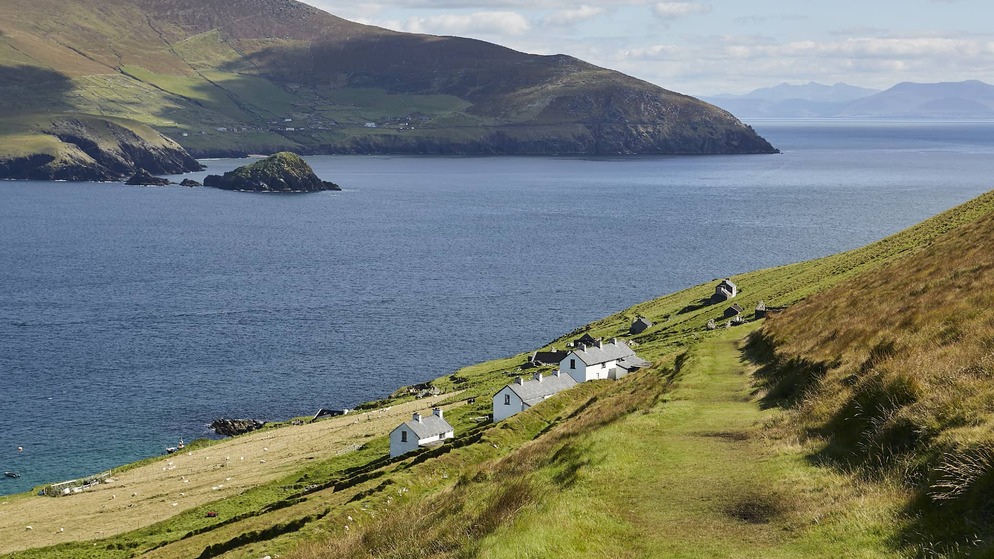 Uitzicht op de Blasket Islands en het vasteland van Kerry, met stenen huisjes verspreid over de heuvel en kalme Atlantische wateren eronder.