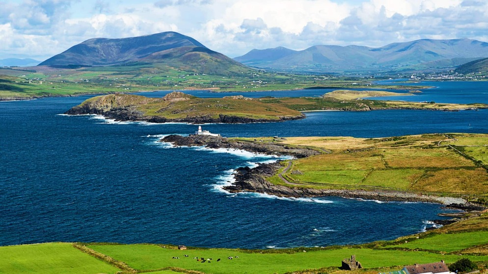 Een vuurtoren op Valentia Island staat op een rotsachtige kaap, omgeven door het blauwe water van de Atlantische Oceaan en de glooiende groene heuvels van Kerry.