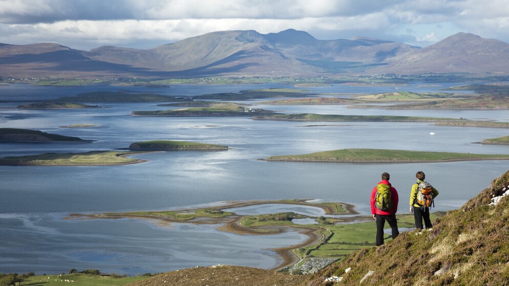 Two hikers look across Clew Bay in County Mayo, dotted with islands and backed by the Nephin Beg mountains.