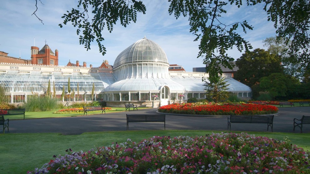 La Palm House, con su cúpula de cristal, en el Jardín Botánico de Belfast, rodeada de céspedes, bancos y coloridos macizos de flores.