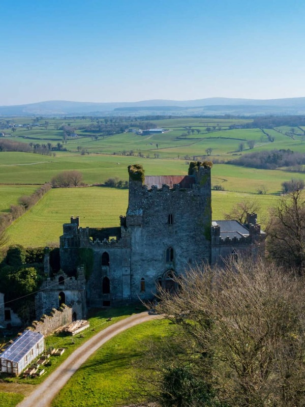 Leap Castle rising above green fields and rolling hills in County Offaly under a clear blue sky.