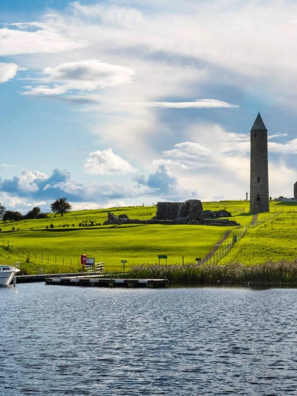 Boat docked by Devenish Island with round tower and ruins in County Fermanagh.