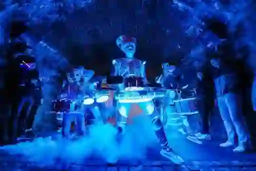 Gekostumeerde straatartiesten die tijdens een Halloween-evenement in Derry op verlichte trommels spelen in een stenen boog.