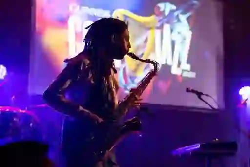 Saxofonist die optreedt op het podium van het Cork Jazz Festival, met kleurrijke verlichting en een festivalscherm achter hem.