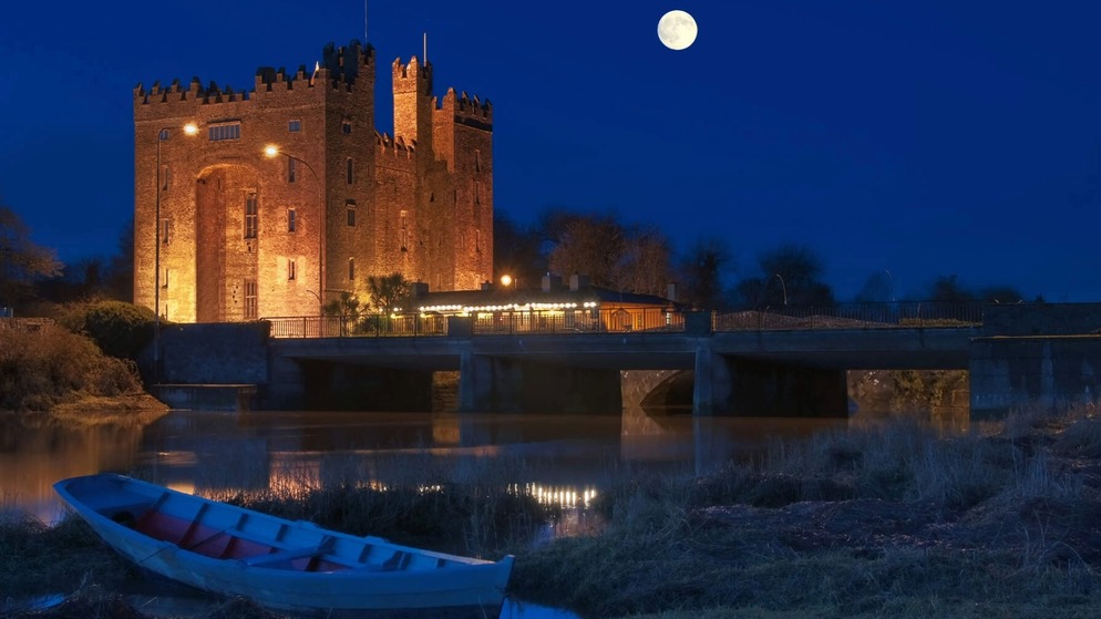 Schloss Bunratty bei Nacht beleuchtet, neben dem Fluss Shannon in der Grafschaft Clare, Irland.