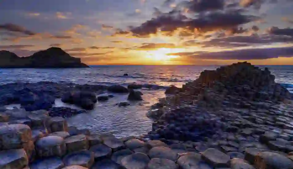 Hexagonal basalt columns at the Giant's Causeway in County Antrim, with waves washing against the rocks beneath a golden sunset.