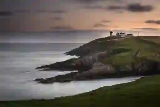 Galley Head Lighthouse on a grassy headland in County Cork, overlooking the Atlantic Ocean and rocky coastline at dusk.
