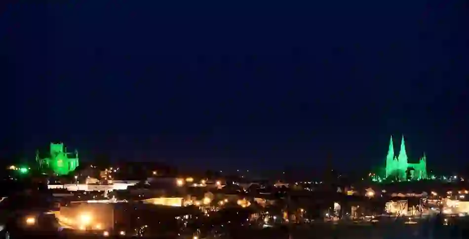 Armagh skyline at night with St Patrick’s Cathedrals illuminated in green above the city.