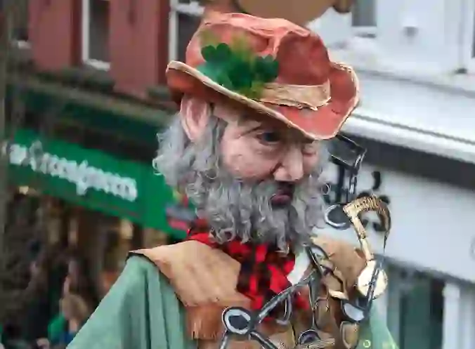 Artista di strada in costume con una grande maschera, cappello a forma di trifoglio e note musicali durante il festival di San Patrizio a Enniskillen.