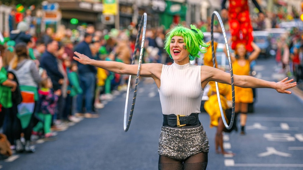 Three performers in colourful wigs and painted faces smile during a St Patrick’s Day parade in Ireland.