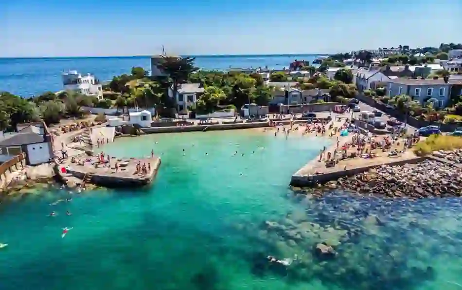 Swimmers and sunbathers enjoy the clear blue water and beach at the Forty Foot bathing spot.